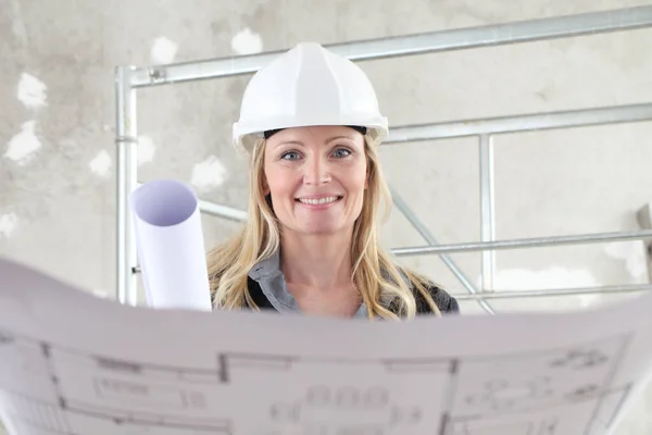 在以脚手架为背景的建筑工地上 一位面带微笑的女建筑师或建筑工程师正在阅读设计图 — 图库照片