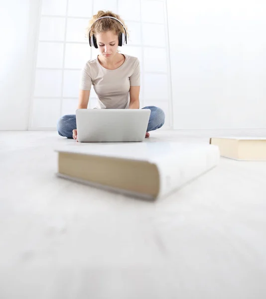 거실에 앉아서 헤드폰과 컴퓨터를 가지고 공부하는 여자는 집안의 개념을 — 스톡 사진
