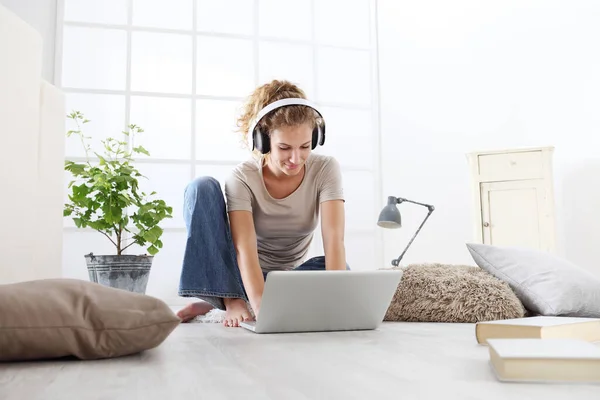 거실에 앉아서 헤드폰과 컴퓨터를 가지고 공부하는 여자는 집안의 개념을 — 스톡 사진
