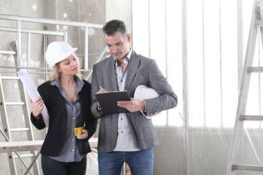 Erkek ve kadın mimarlar ya da mühendisler klasör, plan ve miğfer ile inşaat alanında birlikte çalışıyorlar.