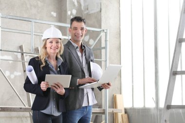 gülümseyen erkek ve kadın mimarlar veya bilgisayar kullanan mühendisler inşaat alanında birlikte çalışıyorlar.