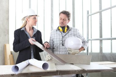 Erkek ve kadın mimar iç mimar ve ustabaşı işçilerle birlikte fayans örnekleri ve dekoratif malzemelerle inşaat alanındaki iç dekorasyon projesini tartışıyorlar.