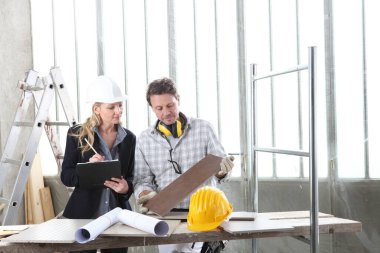 Erkek ve kadın mimar iç mimar ve ustabaşı işçilerle birlikte fayans örnekleri ve dekoratif malzemelerle inşaat alanındaki iç dekorasyon projesini tartışıyorlar.