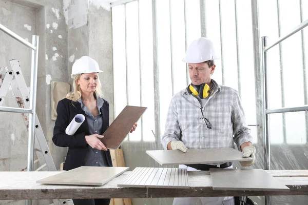 man and woman architect interior designer and foreman worker together with tiles samples and decorative materials discussing the project for interior decoration in the inside the construction building site