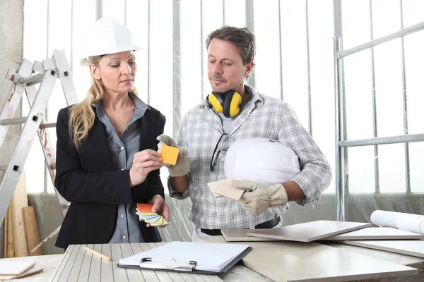 man and woman architect interior designer and foreman worker together with tiles samples and decorative materials discussing the project for interior decoration in the inside the construction building site