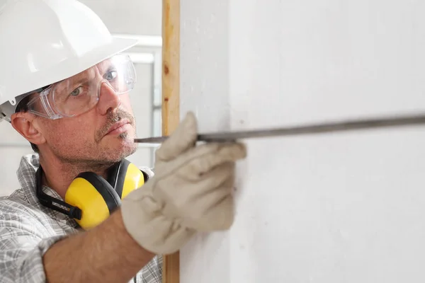 建筑工地男工测量墙角 带正方形帽 眼镜和听觉保护耳机 — 图库照片