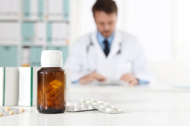 İlaç, su toplaması, şişe ve tablet kutuları resepsiyonda, arka planda doktorla birlikte.