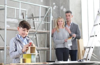 Mutlu çocuklar ve ailesi iç mekanda inşaat modelleriyle bir ev inşa etme oyunu oynuyorlar. Ev satın alma ve bina hedefi kavramı