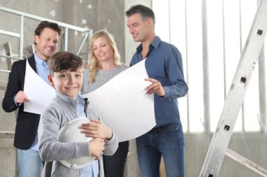 Gülümseyen mutlu çocuğu olan bir aileye ev tasarımı planları gösteren bir mimar. Ev inşaatı hedef kavramı. Ev görünümü, iç dekorasyon ve ev dekorasyonu hakkında konuşmak için iç inşaat sahasında toplantı.