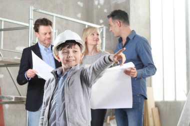 Ev dekorasyonu ve ev dekorasyonu hakkında konuşmak için iç inşaat sahasında toplanan ve çocuk tarafından ev yapımı hedef konsepti olarak gösterilen bir aileye ev tasarımı planları gösteren mimar