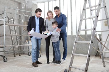 Mimar, çocuklu bir aileye ev tasarımı planlarını gösteriyor. Ev görünümü, iç dekorasyon, ev düzeni ve duvar renkleri hakkında konuşmak için iç inşaat sahasında toplantı.