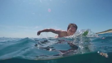 Yavaş hareket sualtı: açık deniz okyanus bir sörf üzerinde kürek çekmeye genç sörfçü adam