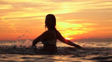 Ağır çekim: çekici genç kız okyanus su ile altın günbatımında oynamaktan