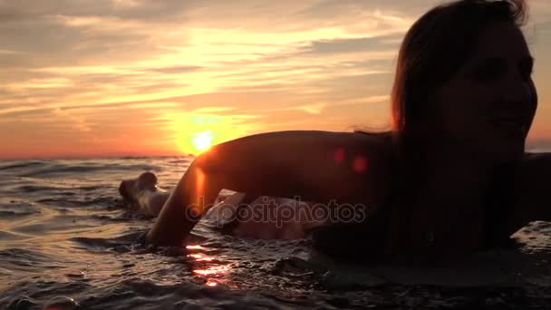 FECHAR-se: Menina alegre bonita remando na prancha de surf no pôr do sol dourado — Vídeo de Stock