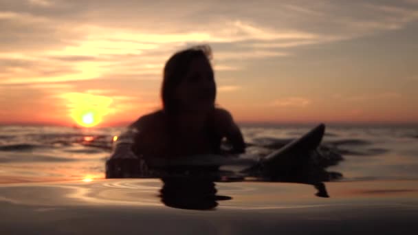 Молодая весёлая девушка гремит в глубоком океане на доске для серфинга на золотом закате — стоковое видео