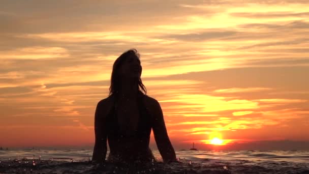 Zeitlupe: Schönes junges Mädchen, das bei goldenem Sonnenuntergang Wasser in den Ozean gießt — Stockvideo