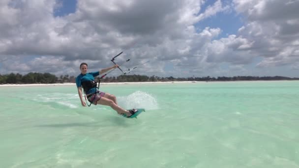 Αργή κίνηση: Χαμογελαστός surfer κορίτσι kitesurfing παρελθόν την κάμερα στη γαλάζια λιμνοθάλασσα — Αρχείο Βίντεο