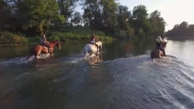 Yakın: güneşli günde nehre ata binerek üç neşeli kız