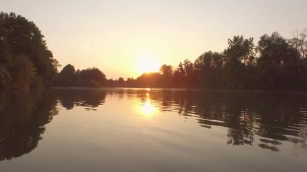 AEREO, CHIUSO: Superficie fluviale lucida che riflette il cielo dorato e la riva lussureggiante — Video Stock