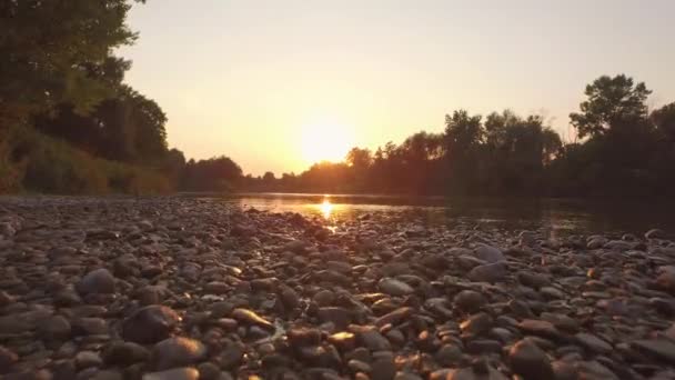 AERIAL, CERRAR: Ribera rocosa y superficie de agua que refleja el cielo dorado — Vídeos de Stock