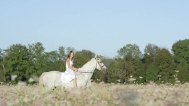 Ağır çekim: Beyaz elbiseli çiçek açan alanındaki beyaz at binme eyersiz kız