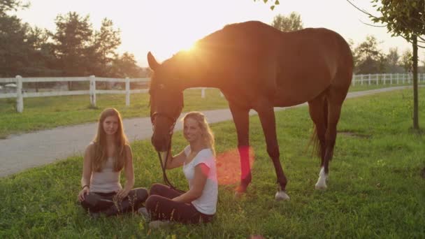 Movimiento lento: Dos niñas sentadas en la hierba y pasando el rato y acariciando a caballo — Vídeo de stock