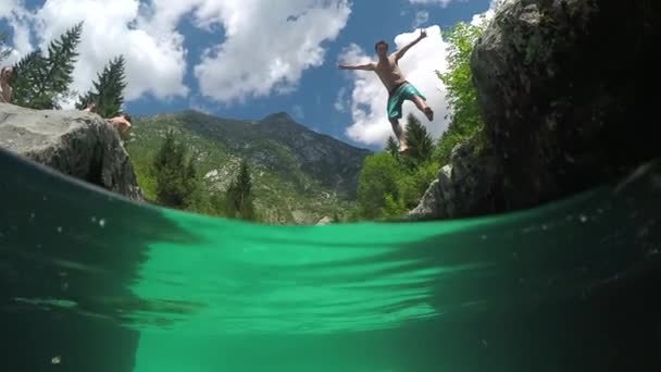 CLOSE UP: Smiling man jumping with hand raised into amazing crystal clear water — 图库视频影像