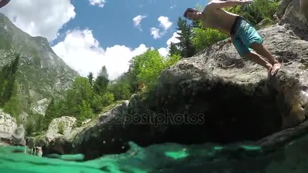 CLOSE UP: Smiling man jumping with hands raised into refreshing clear river — Stock Video