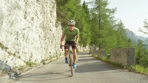 SLOW MOTION: Homem atlético caucasiano pedalando sua bicicleta de estrada até uma colina íngreme . — Vídeo de Stock