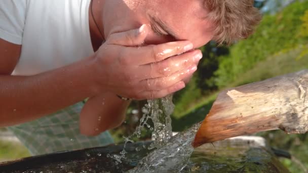 Посміхаючись молодий чоловік бризкає освіжаючою струмковою водою на обличчі . — стокове відео