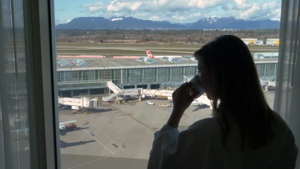 LOSE UP: vrouw in badjas thee drinken en kijken naar de luchthaven terminal hieronder — Stockvideo