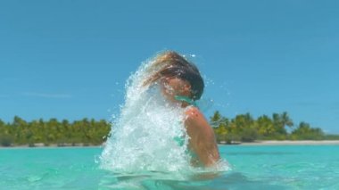 Uzun kahverengi saçlarıyla deniz suyunu sıçratan mutlu turist kız..