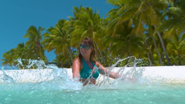 CLOSE UP: Весела молода жінка обприскує скляну океанську воду руками . — стокове відео