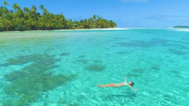 AERIAL: Zorgeloos meisje op vakantie zwemmen op haar rug in de buurt van het tropische eiland. — Stockvideo