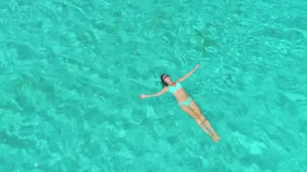 AERIAL: Mujer acostada boca arriba en la tranquila superficie del océano turquesa. — Vídeo de stock