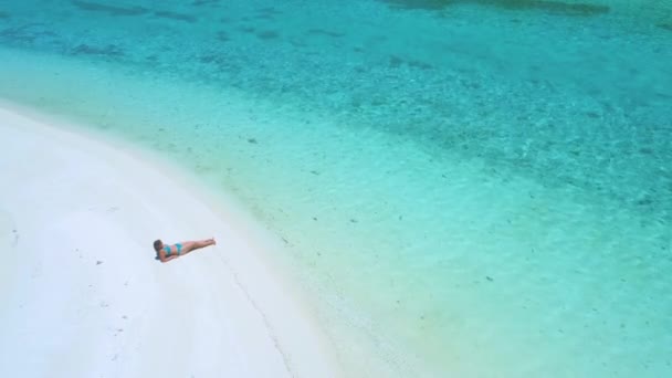 AERIAL: Junge Frau liegt am Strand und sonnt sich am türkisfarbenen Meer. — Stockvideo