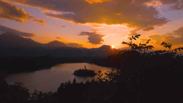 Drone: Oranje zonsopgang verlicht het rustige meer Bled onder de bergen — Stockvideo