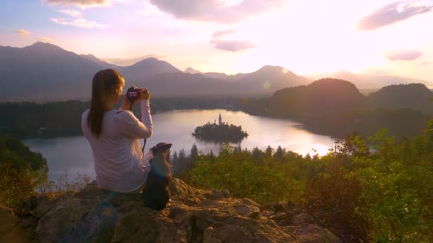 ESPACIO DE COPIA: Chica viajera sentada junto a su cachorro y tomando fotos de la puesta del sol . — Vídeos de Stock