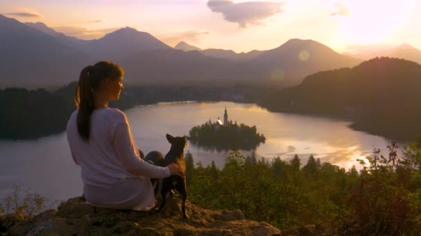 귀여운 개와 함께 아래에 있는 아름다운 호수를 바라보고 있는 젊은 여자와 가까이서 — 비디오
