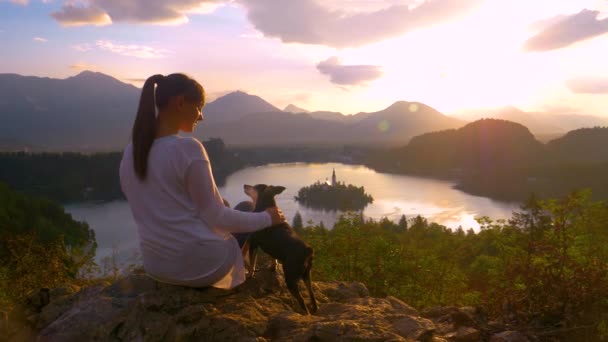 Gölün yukarısındaki bir kayanın üzerinde oturan dişi turist kanadı ve köpeğini okşadı.. — Stok video