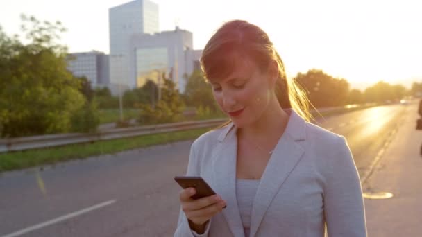 LOSE UP: Leende affärskvinna sms när du går ner trottoaren vid soluppgången. — Stockvideo