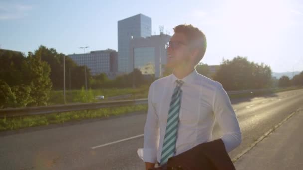CLOSE UP: Усміхнений бізнесмен, здається, загубився і оглядається навколо сонячного міста — стокове відео