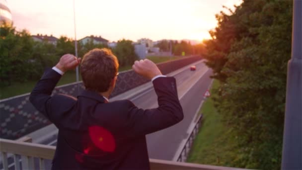 SLOW MOTION: Cheerful businessman outstretches his arms while watching sunset. — ストック動画