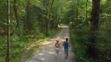 DRONE: Athletic couple jogging down gravel trail running through the woods.