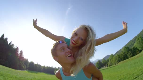 PORTRAIT: Laughing man carries playful girlfriend on his back during their date — Stok video