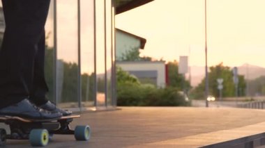 LOW ANGLE: Unrecognizable businessman longboarding through city on sunny evening