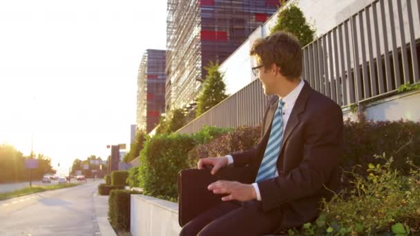 SLOW MOTION: Cheerful businessman sitting on a ledge and singing after promotion — 图库视频影像