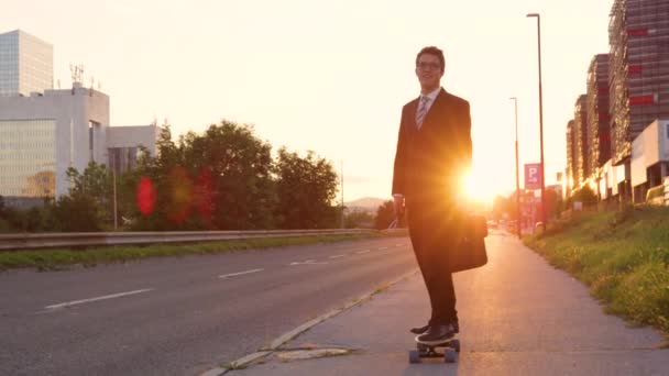 SLOW MOTION: Усміхнений бізнесмен скейтбординг порожнім тротуаром на заході сонця — стокове відео