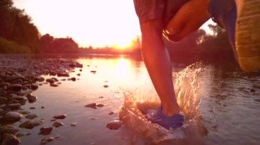 CLOSE UP: Unrecognizable sportsman running in the river shallows at golden hour.