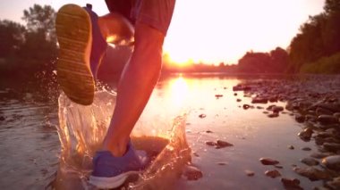 SLOW MOTION: Golden evening sunbeams shine on athletic man jogging along river.